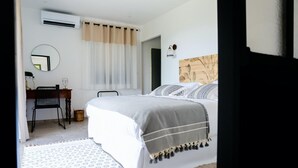 Un dormitorio con cama, escritorio con silla, espejo y aire acondicionado instalado en la pared.