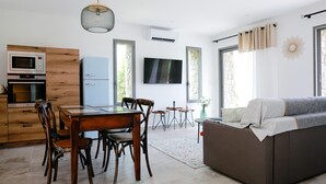 Una cocina moderna con microondas y horno integrados, un comedor con sillas y mesa de madera, y una sala de estar con sofá y televisor.