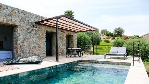Un edificio de piedra con piscina, mobiliario exterior y una pérgola.
