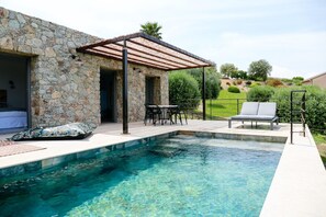 Ein Gebäude aus Stein mit Pool, Sitzmöglichkeiten im Freien und einer Pergola.