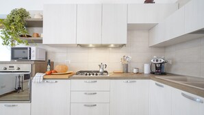 Een moderne keuken met witte kasten, een magnetron, fornuis en diverse keukengerei.