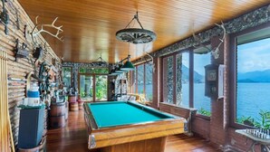 Une salle de billard avec une table de billard, des murs en bois et une vue sur un lac.