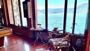 Une pièce dotée d’un plancher en bois, d’une table de billard, d’un coin bar avec une petite table et des tabourets, et de grandes fenêtres offrant une vue sur un lac et des montagnes.
