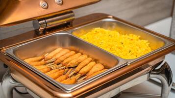 A buffet with two metal serving trays, one containing corn dogs and the other with yellow rice.