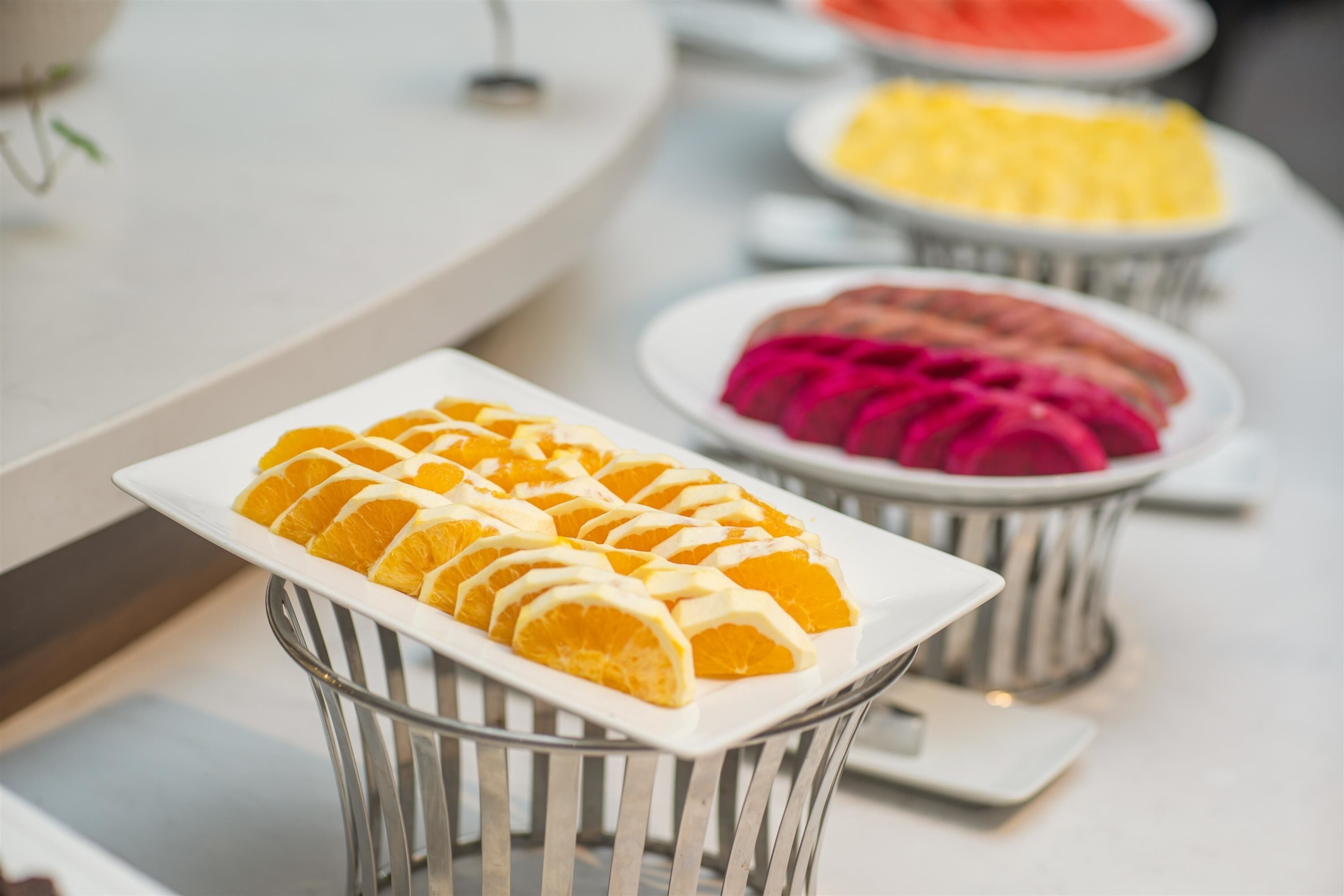 A buffet with neatly arranged fruit slices in metal baskets.