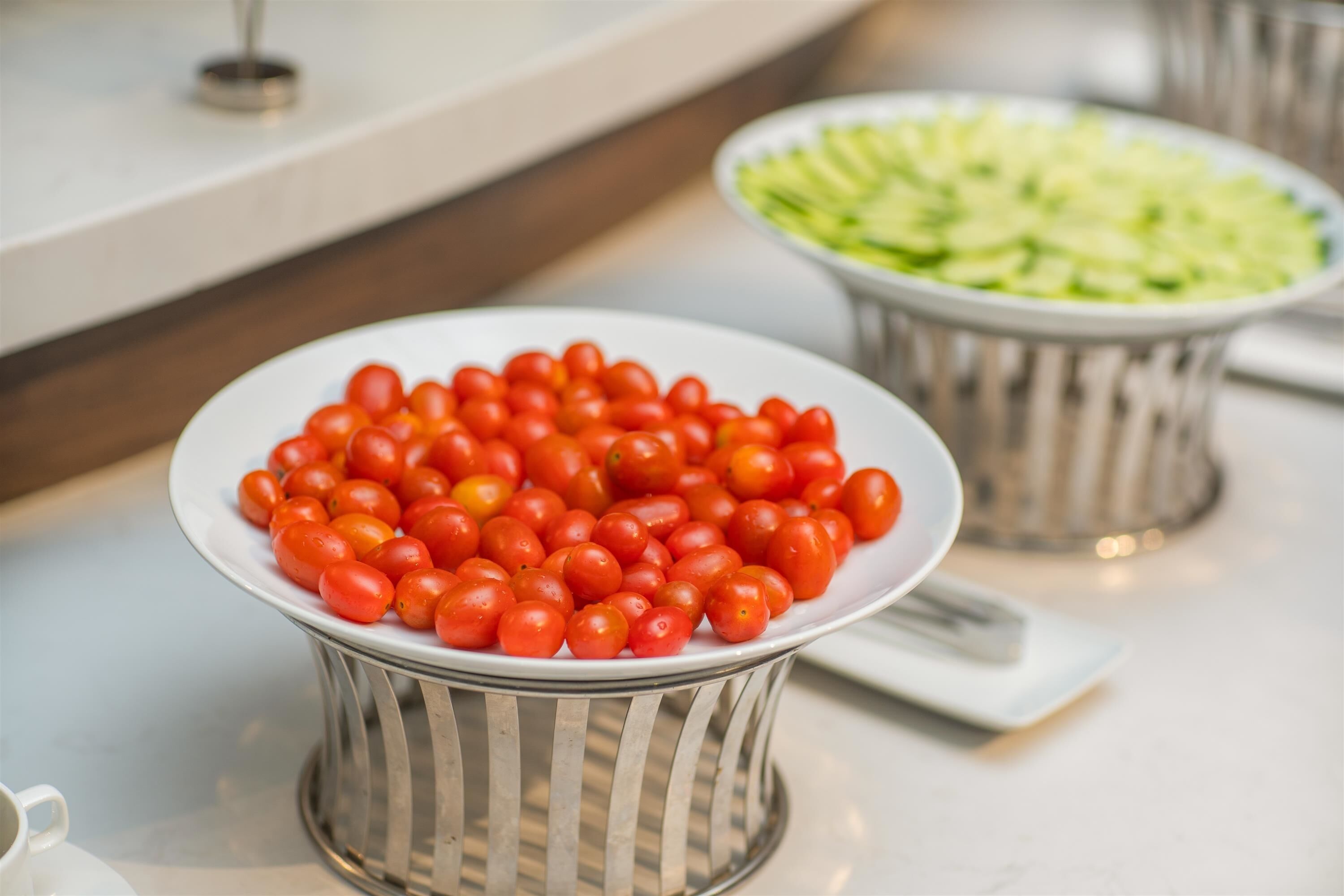A buffet table with a plate of cherry tomatoes and a plate of sliced cucumbers.
