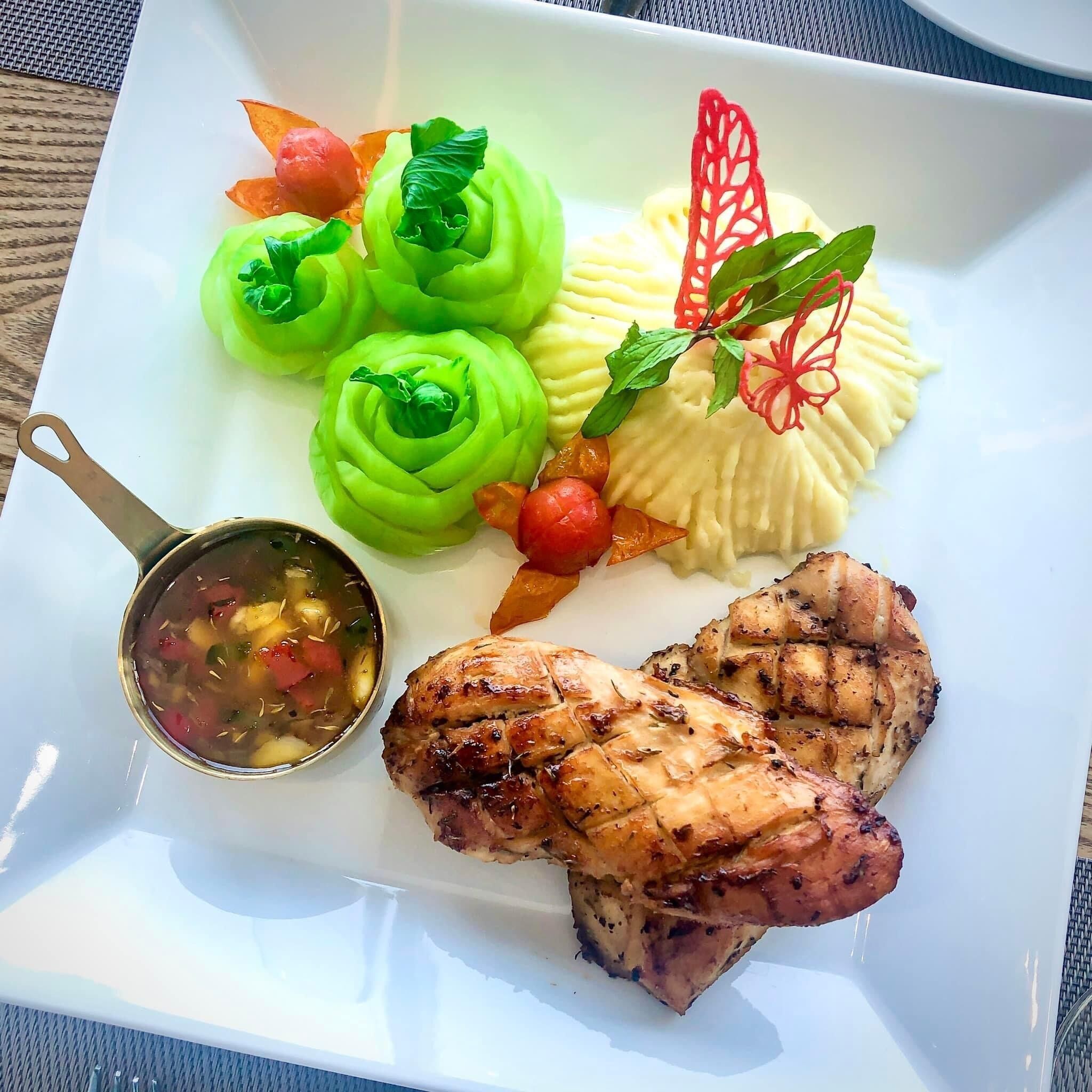 A plate with grilled meat, green vegetable rolls, mashed potatoes, and a small bowl of soup.