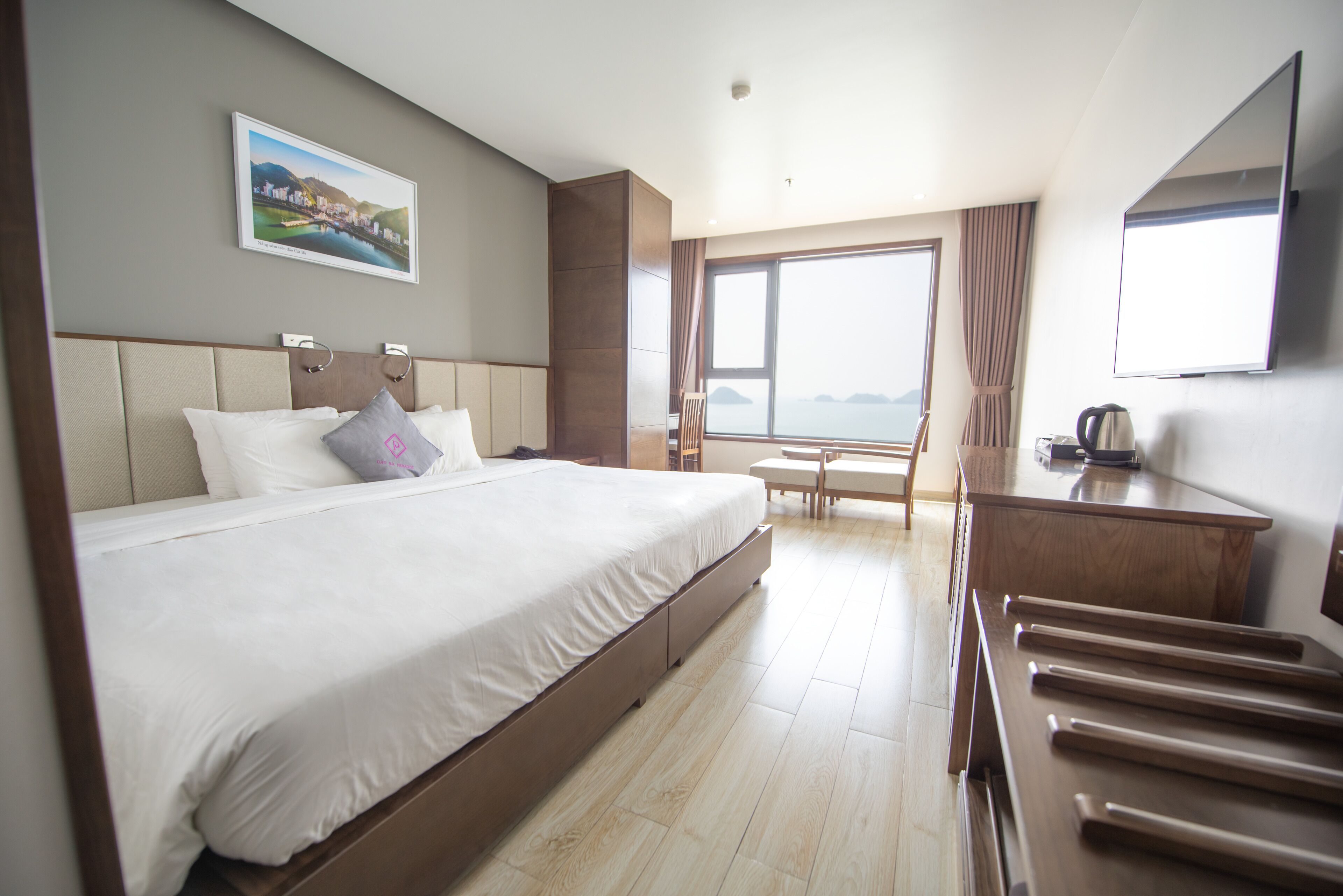 Ein Hotelzimmer mit einem großen Bett, einem Schreibtisch, einem Stuhl, einem Fenster mit Aussicht und einem an der Wand befestigten Fernseher.