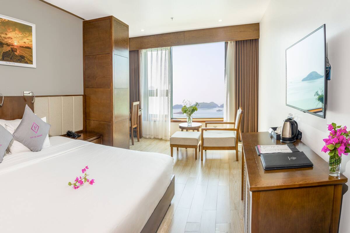 A hotel room with a large bed, a desk with a laptop, a coffee maker, and a view of the sea.