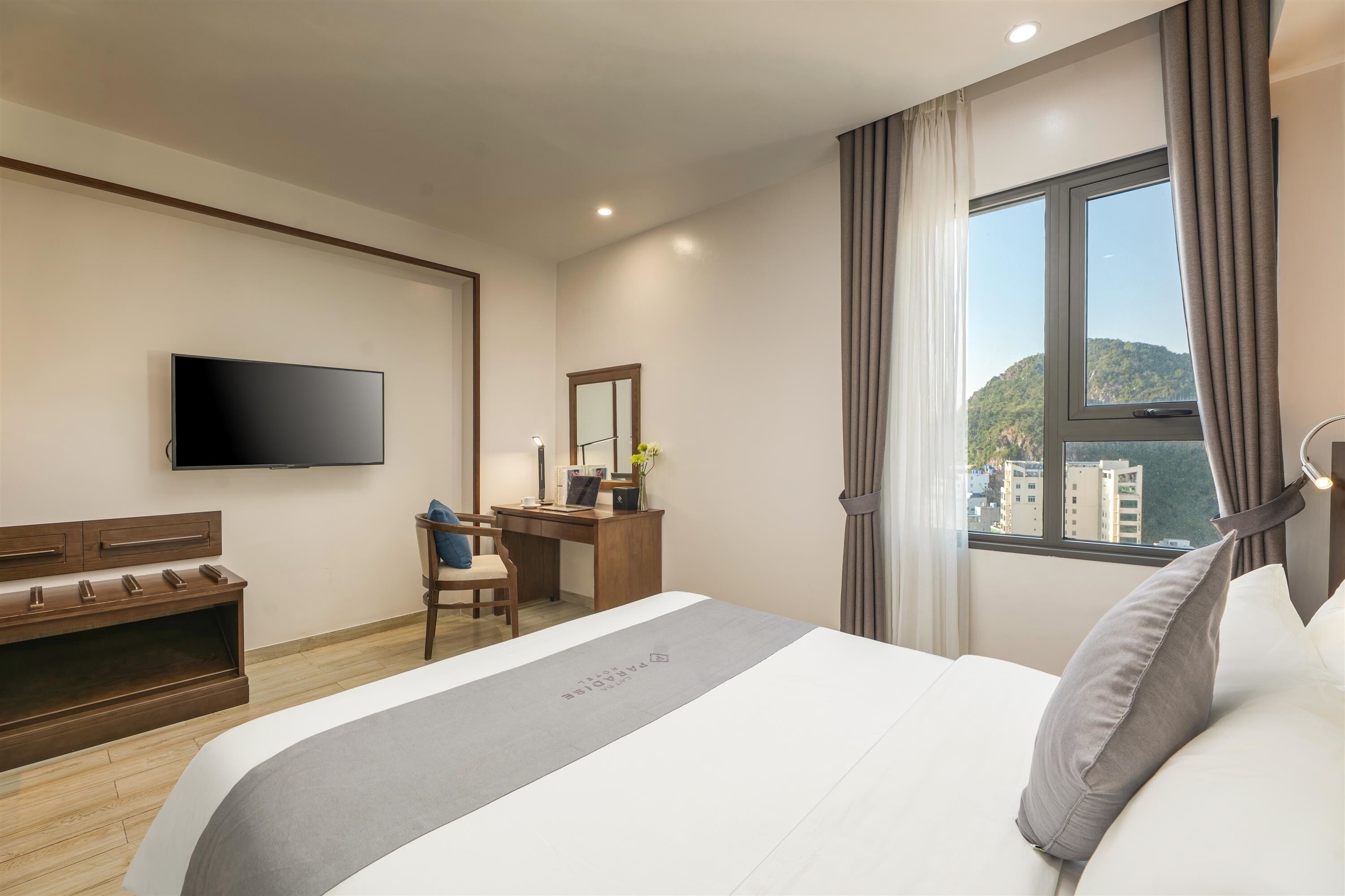 A hotel room with a bed, a desk, a chair, a TV, and a window with a view.