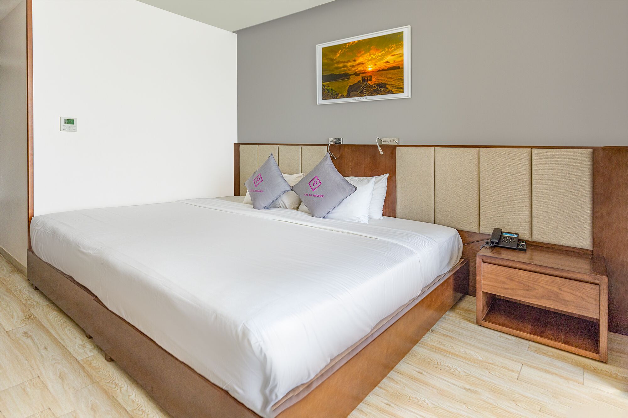 Une chambre d’hôtel avec un grand lit, une tête de lit en bois, une table de chevet avec un téléphone et un tableau encadré au mur.