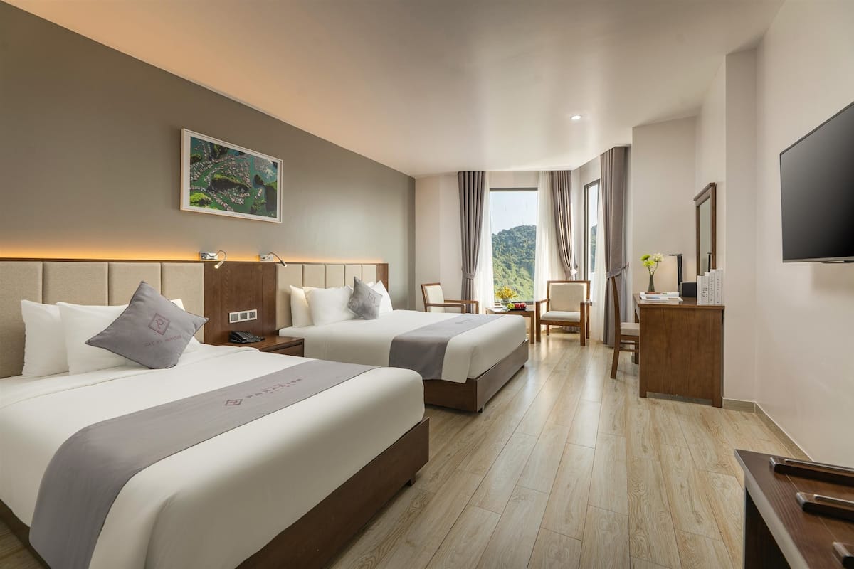 A hotel room with two beds, a desk, a TV, and a window with curtains.