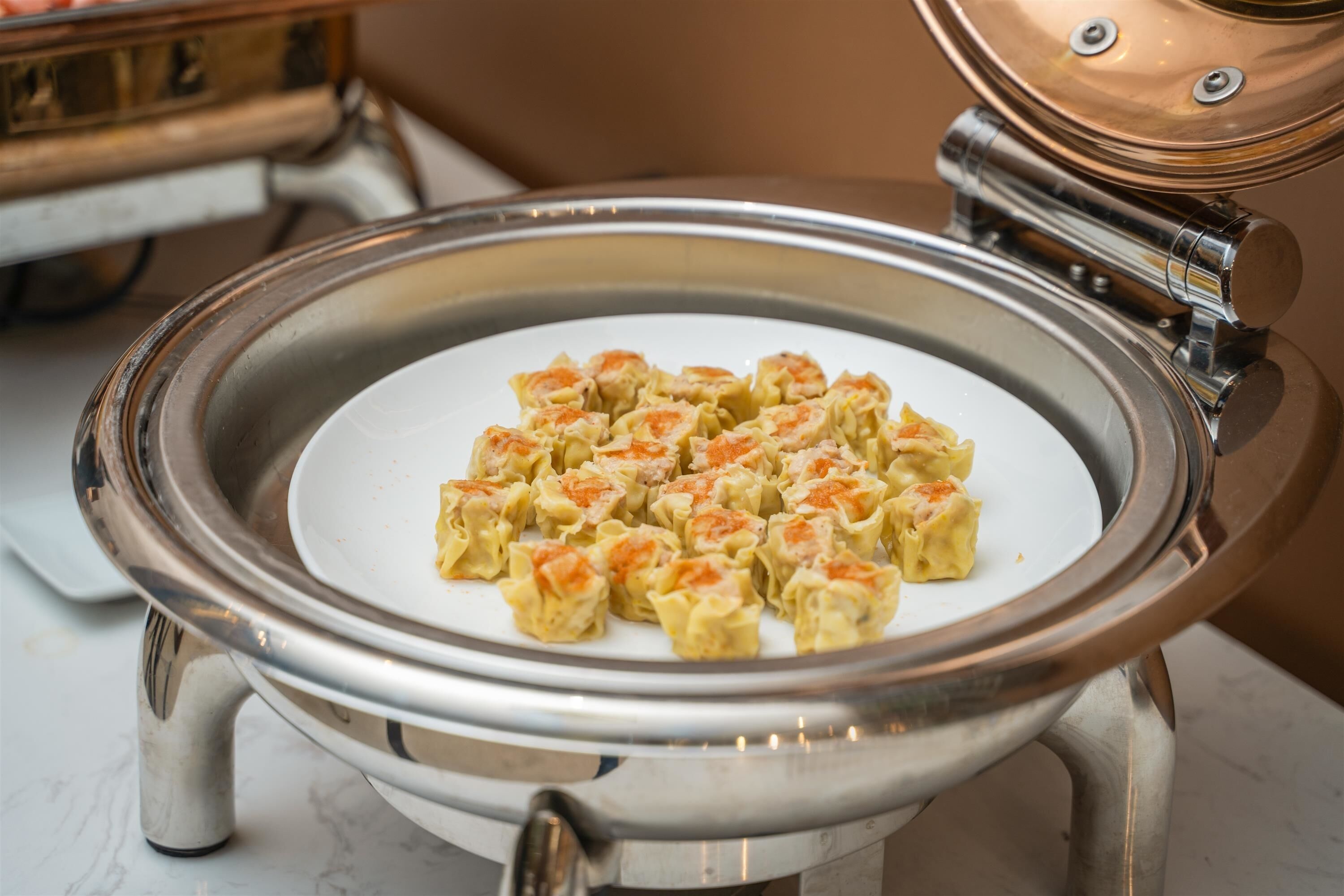 A stainless steel buffet bowl with food items.