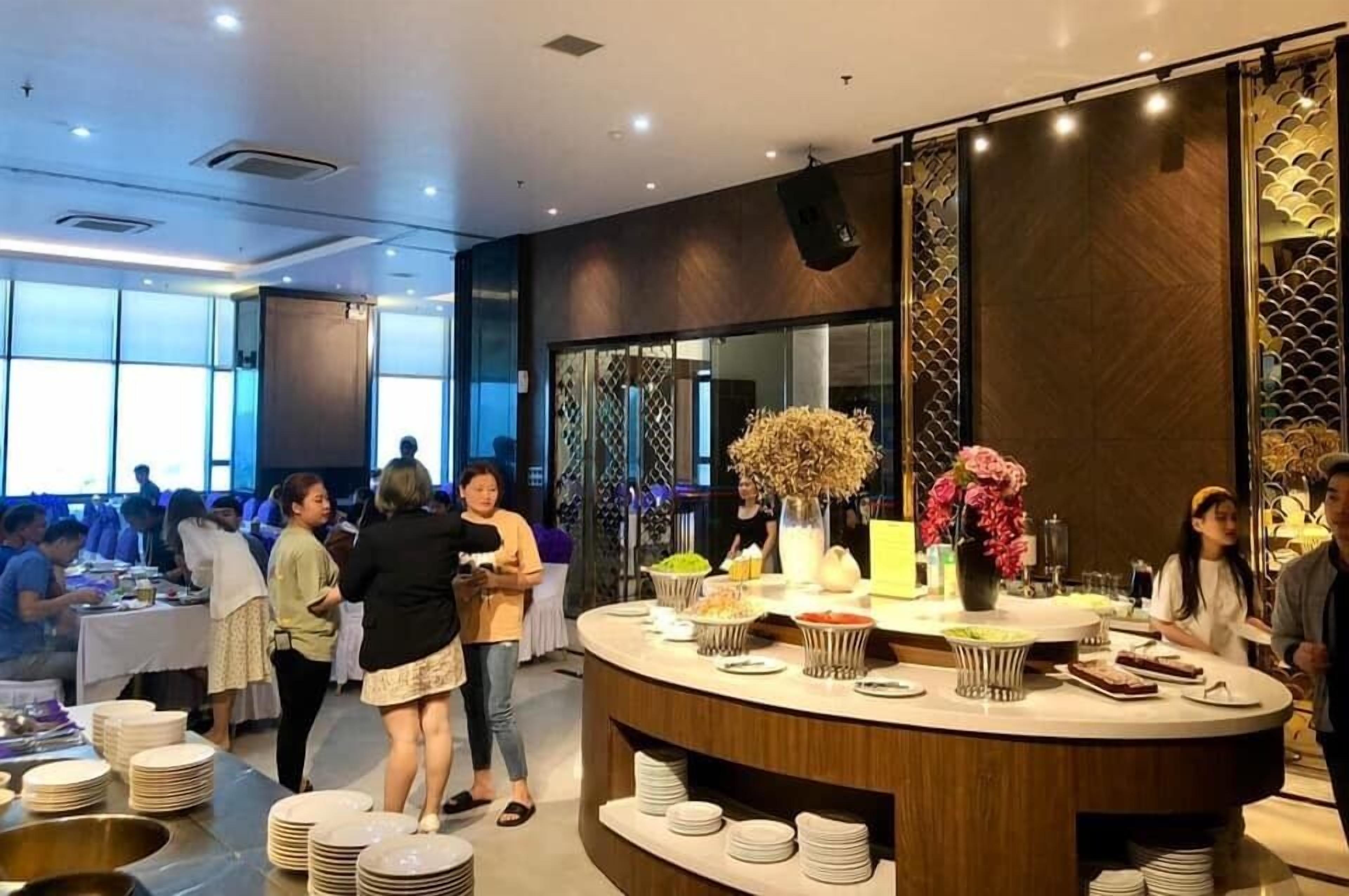 Disposição de buffet com várias estações de serviço, um vaso decorativo central e área de estar com mesas e cadeiras.