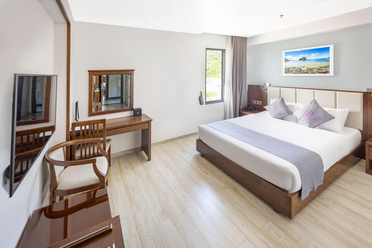 A hotel room with a bed, a desk, a chair, a TV, a window with curtains, and a picture on the wall.