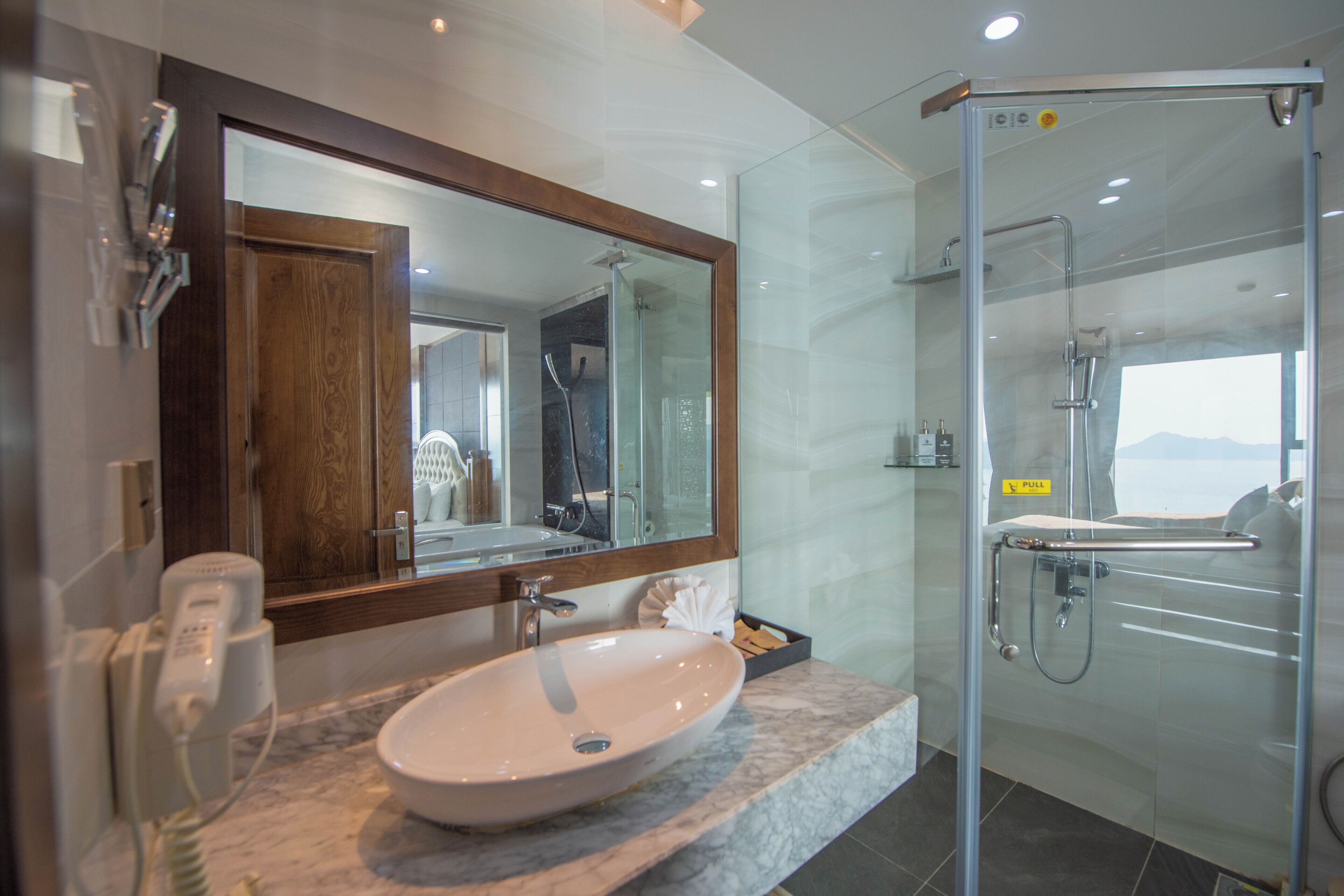 A bathroom with a marble sink, a mirror, a glass shower enclosure, and a view of the mountains.