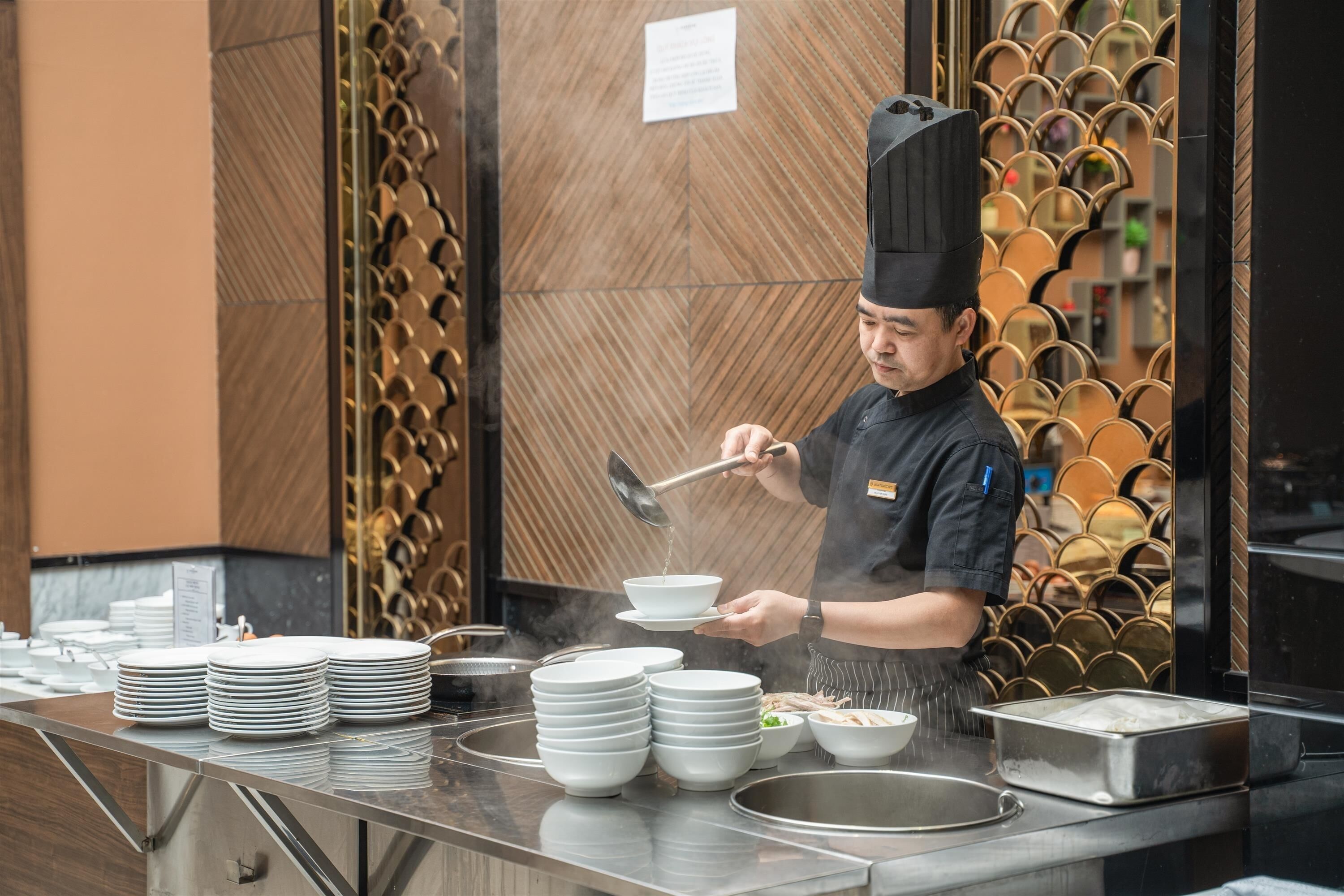 A chef preparing food in a kitchen with a decorative wall and a stack of plates.