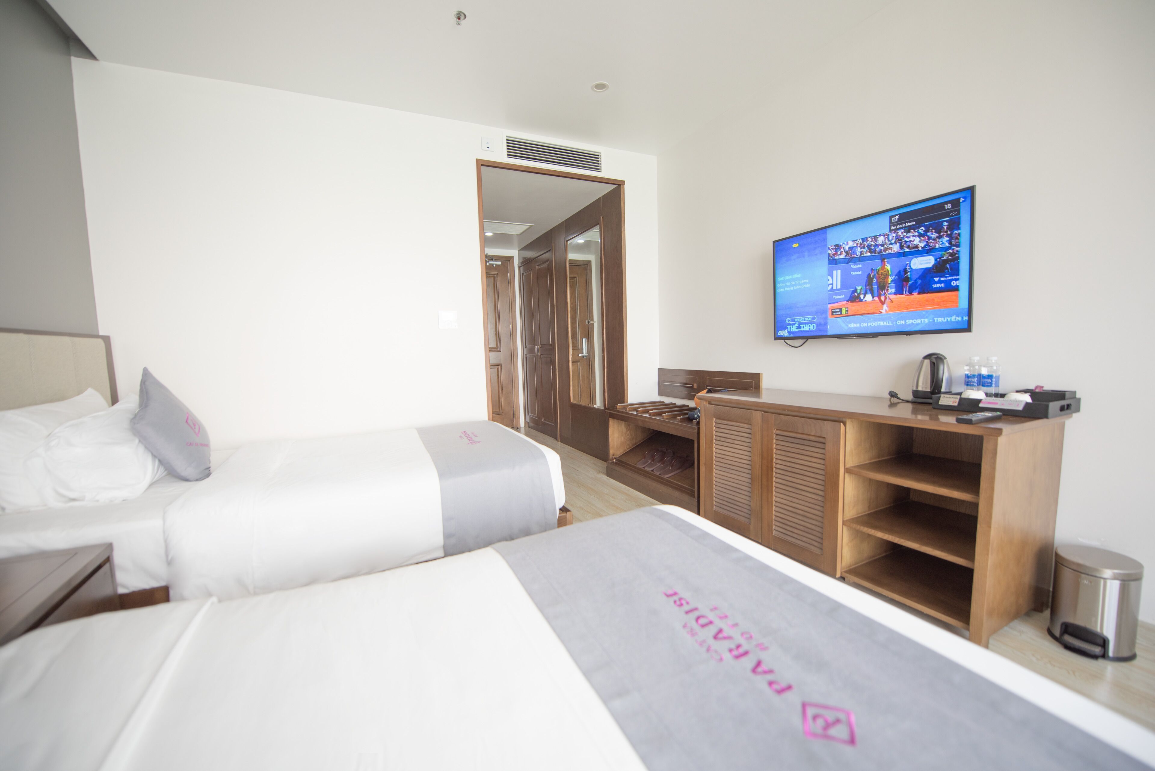 A hotel room with two beds, a TV on the wall, a desk, and a trash can.