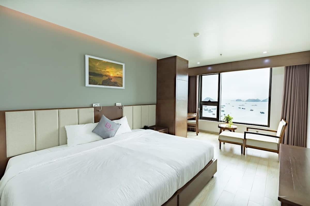 A hotel room with a large bed, a desk, a chair, and a view of the sea.