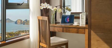 Un escritorio de madera con una laptop, un florero con flores y libros. Una silla está colocada frente al escritorio.