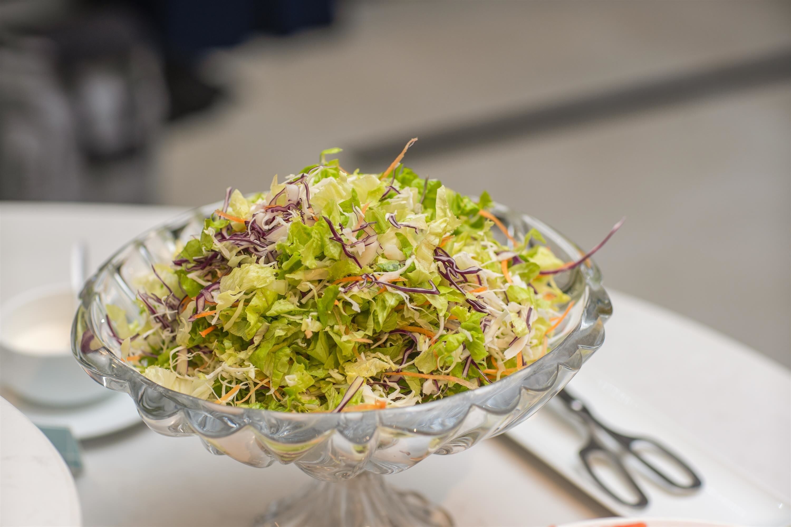 Een glazen kom met een salade op een witte tafel.