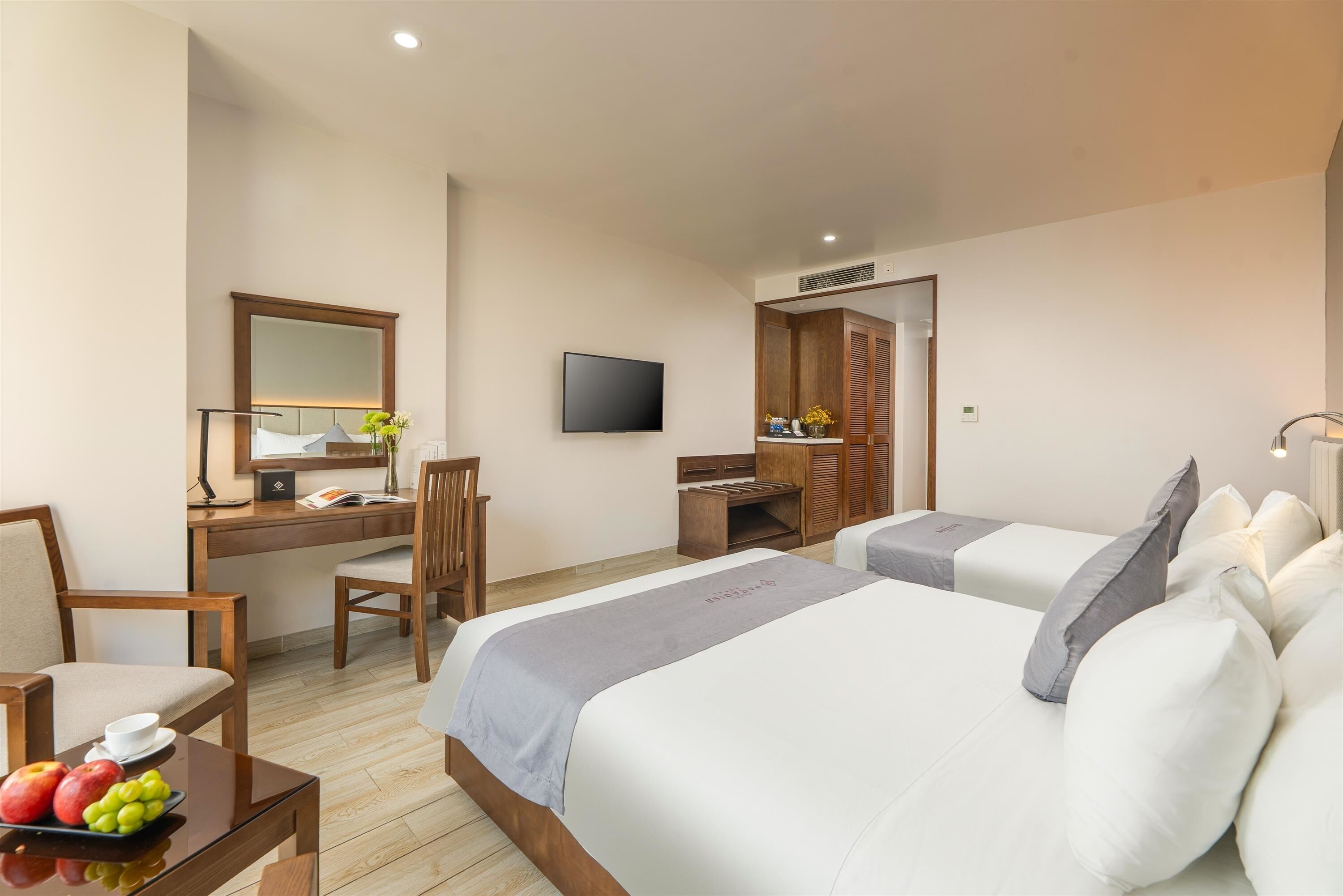 Une chambre d’hôtel avec deux lits, un bureau avec une chaise, une télévision et une petite table avec des fruits.