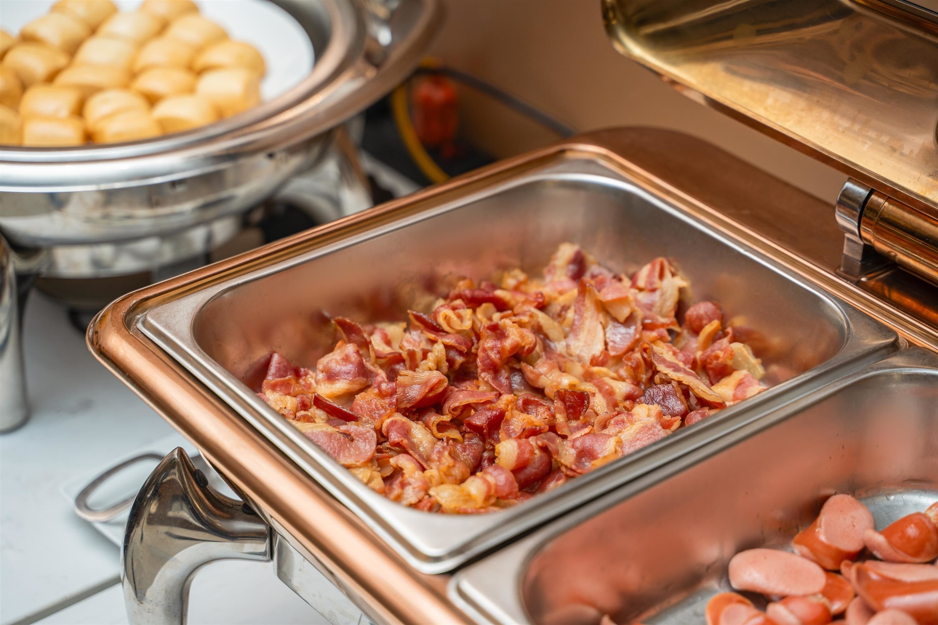 A buffet with various food items, including bacon and sausages.