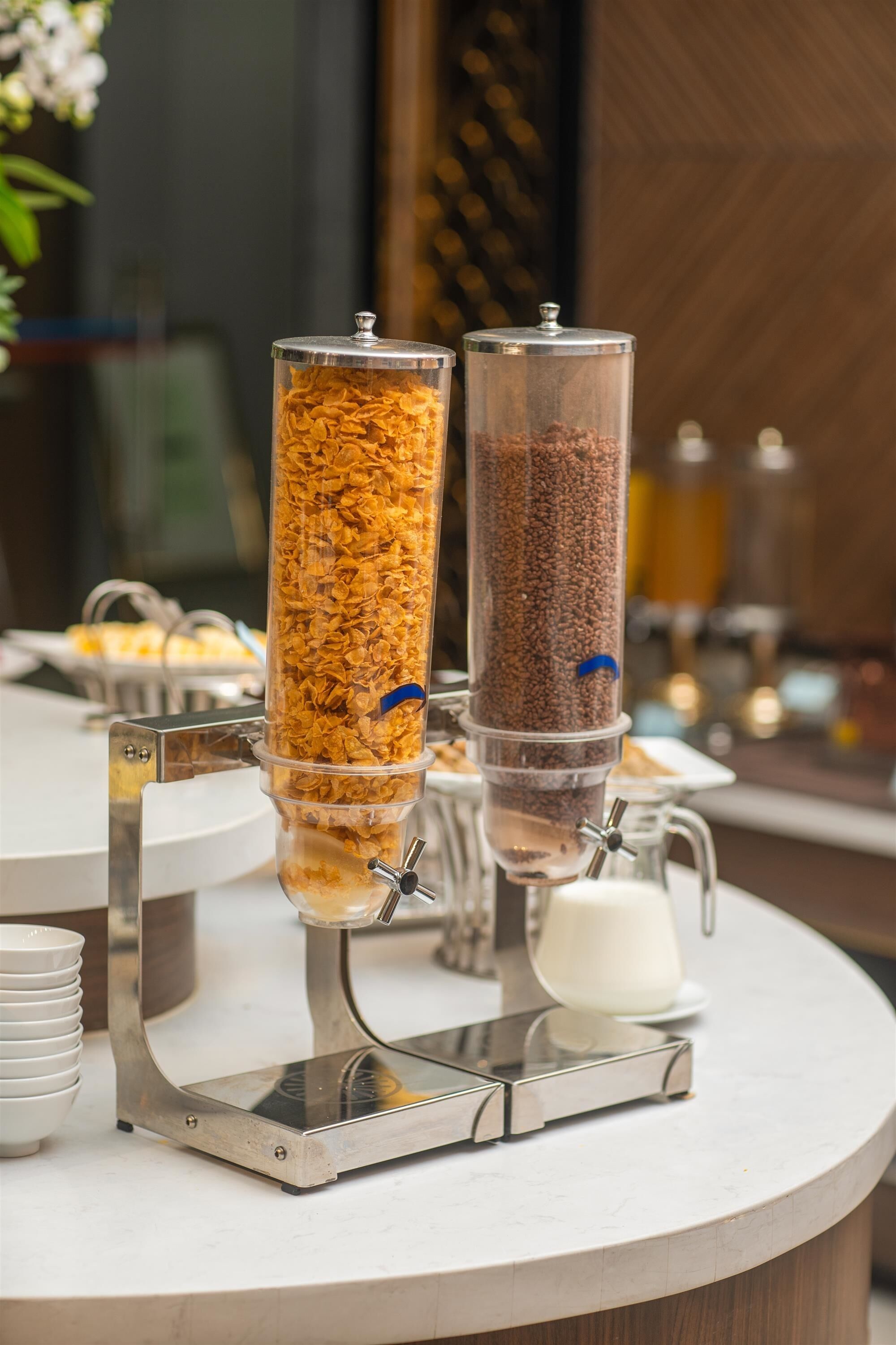 Morgenmadsbuffet med to dispensere, den ene med cornflakes og den anden med granola, på en marmor bordplade.