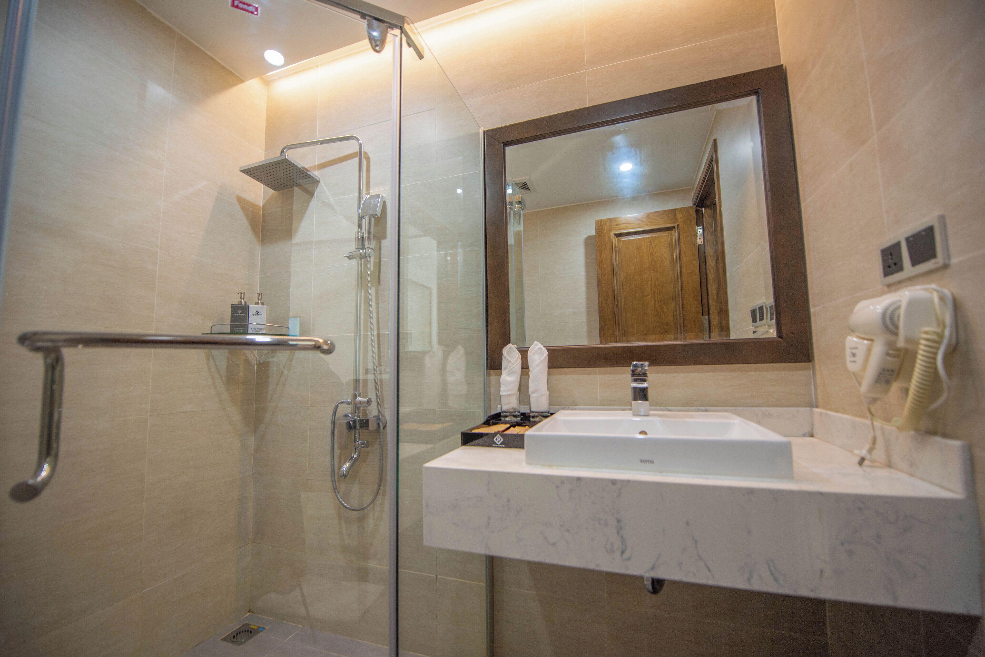Ein modernes Badezimmer mit einer gläsernen Dusche, einem weißen Waschbecken mit Marmorplatte und einem großen Spiegel.