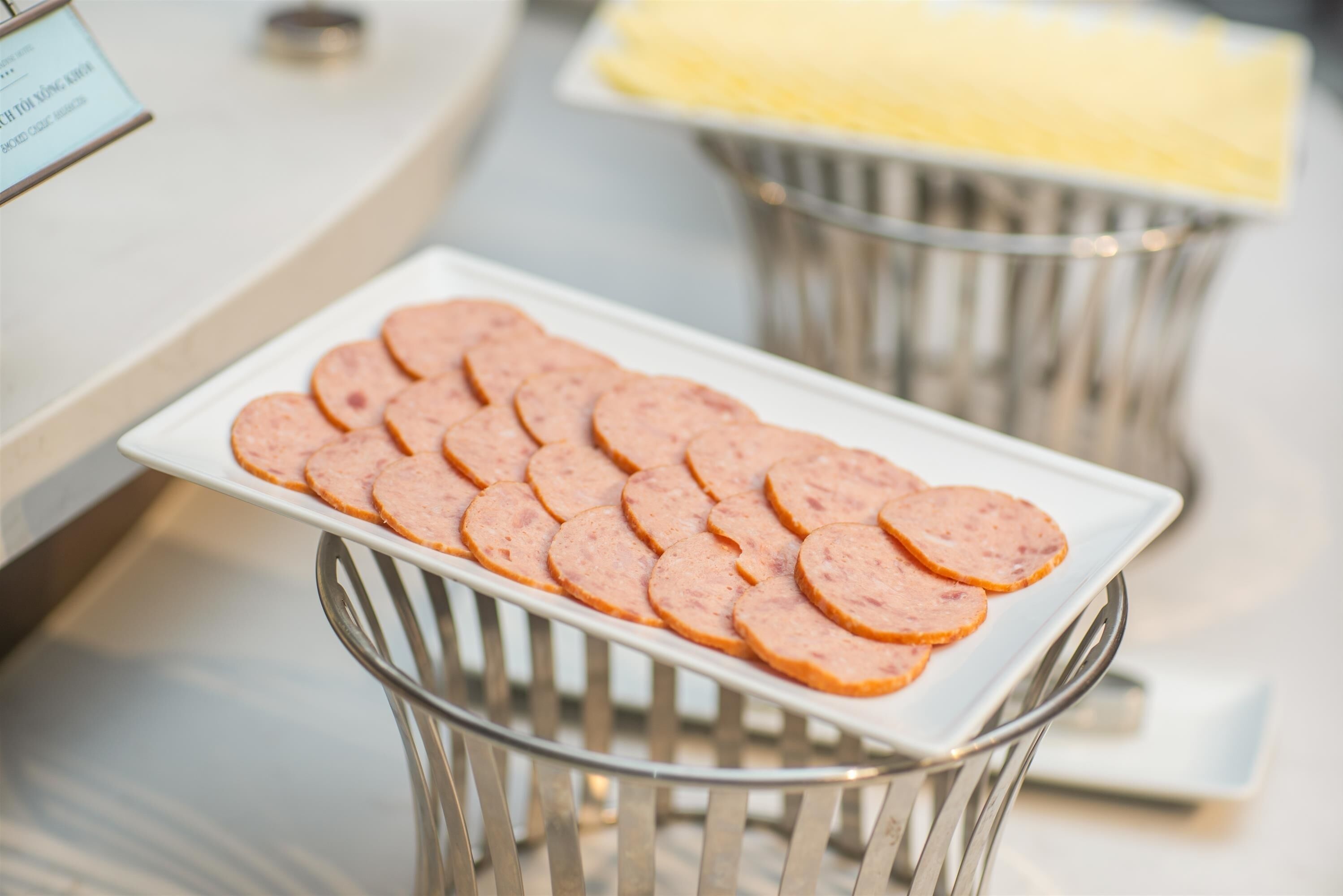 A white plate with sliced sausage on a metal tray.