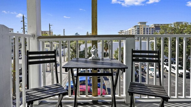 A balcony with two black chairs and a table, a white statue, and a view of parked cars and buildings. - Live-Love-St Pete! Hipster 1 bdrm Studio in DTSP!! (St. Petersburg)