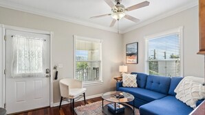 A living room with a blue sofa, a white chair, a coffee table, and a ceiling fan. - Live-Love-St Pete! Hipster 1 bdrm Studio in DTSP!! (St. Petersburg)