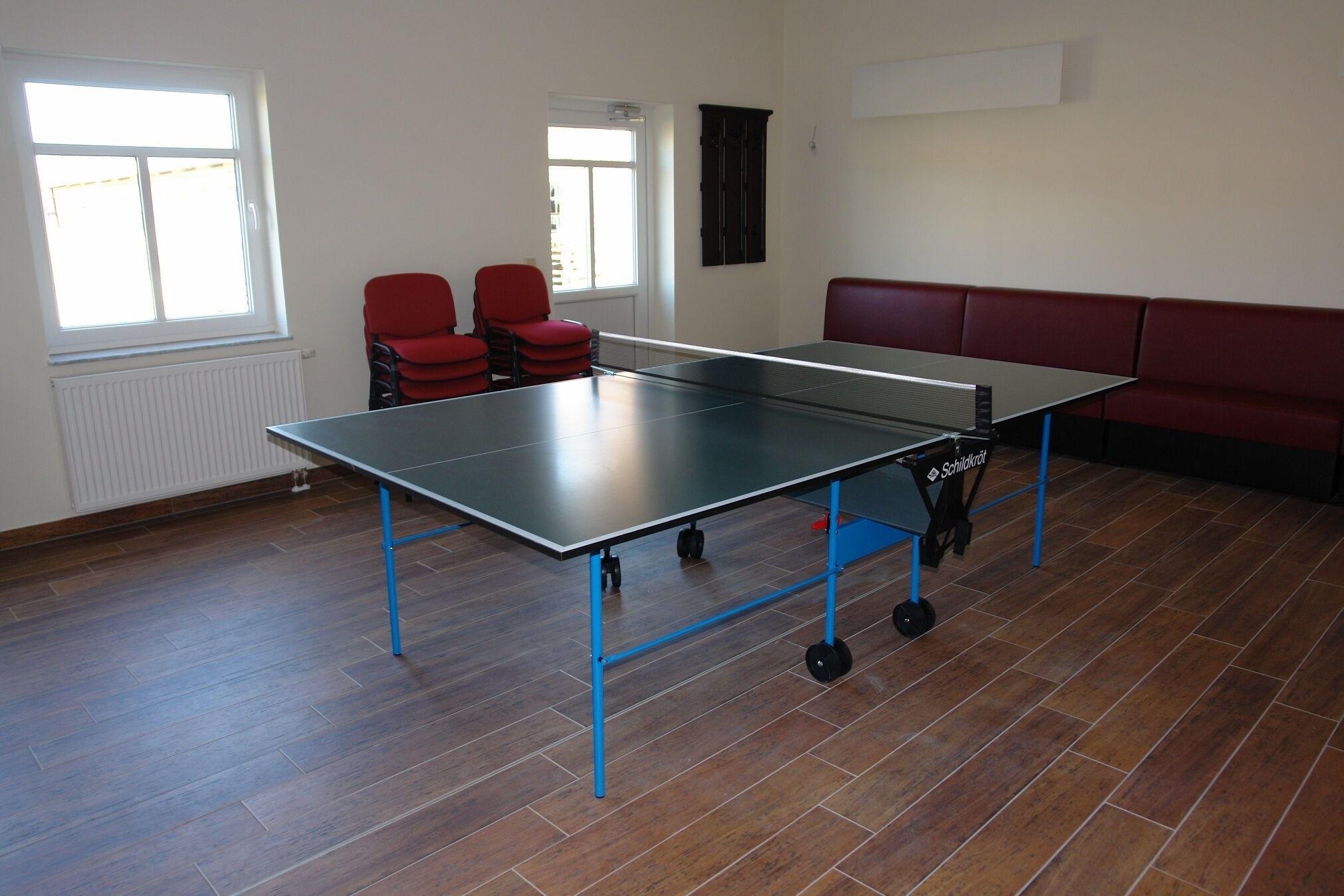 Een tafeltennistafel in een kamer met houten vloeren, een rode bank en twee rode stoelen.