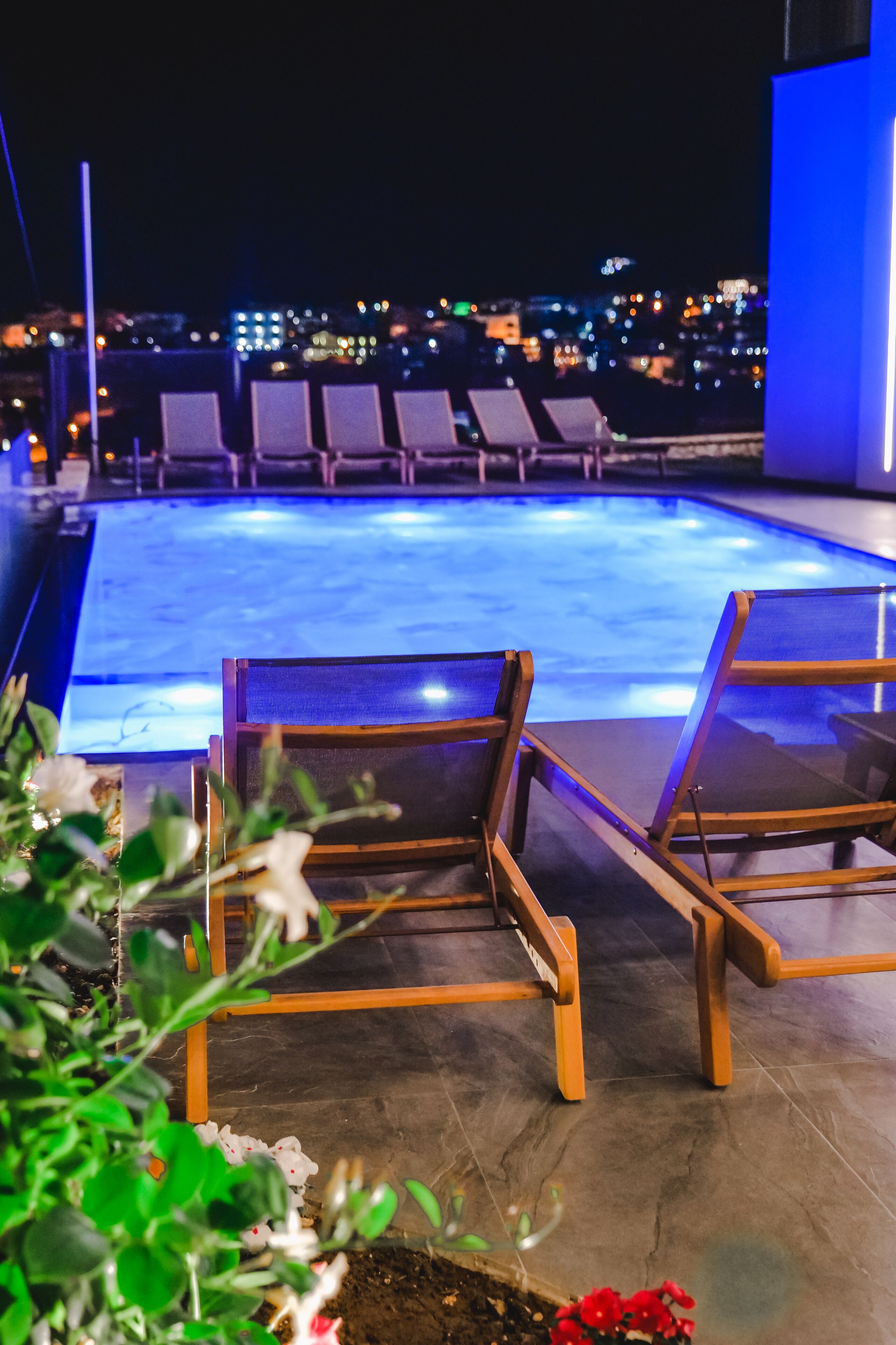 Un área de piscina en la azotea con sillones y vistas nocturnas de la ciudad.