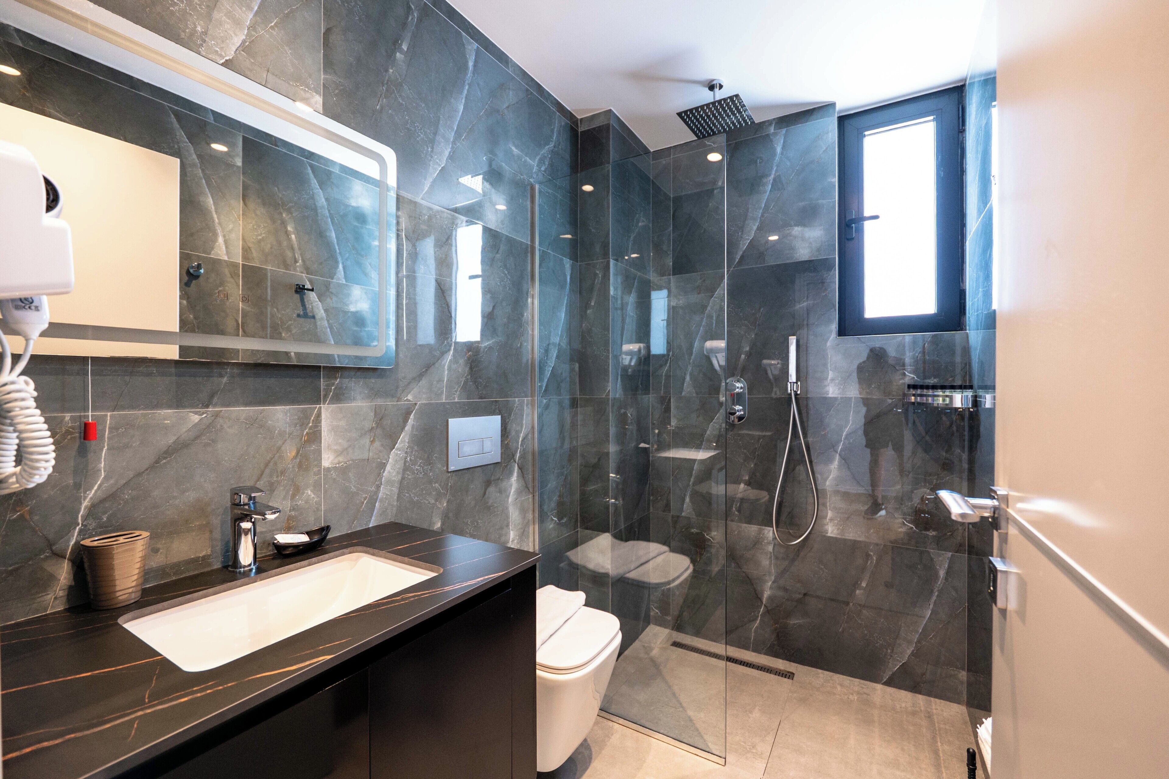 A modern bathroom with a large mirror, a sink, a toilet, and a glass-enclosed shower area.