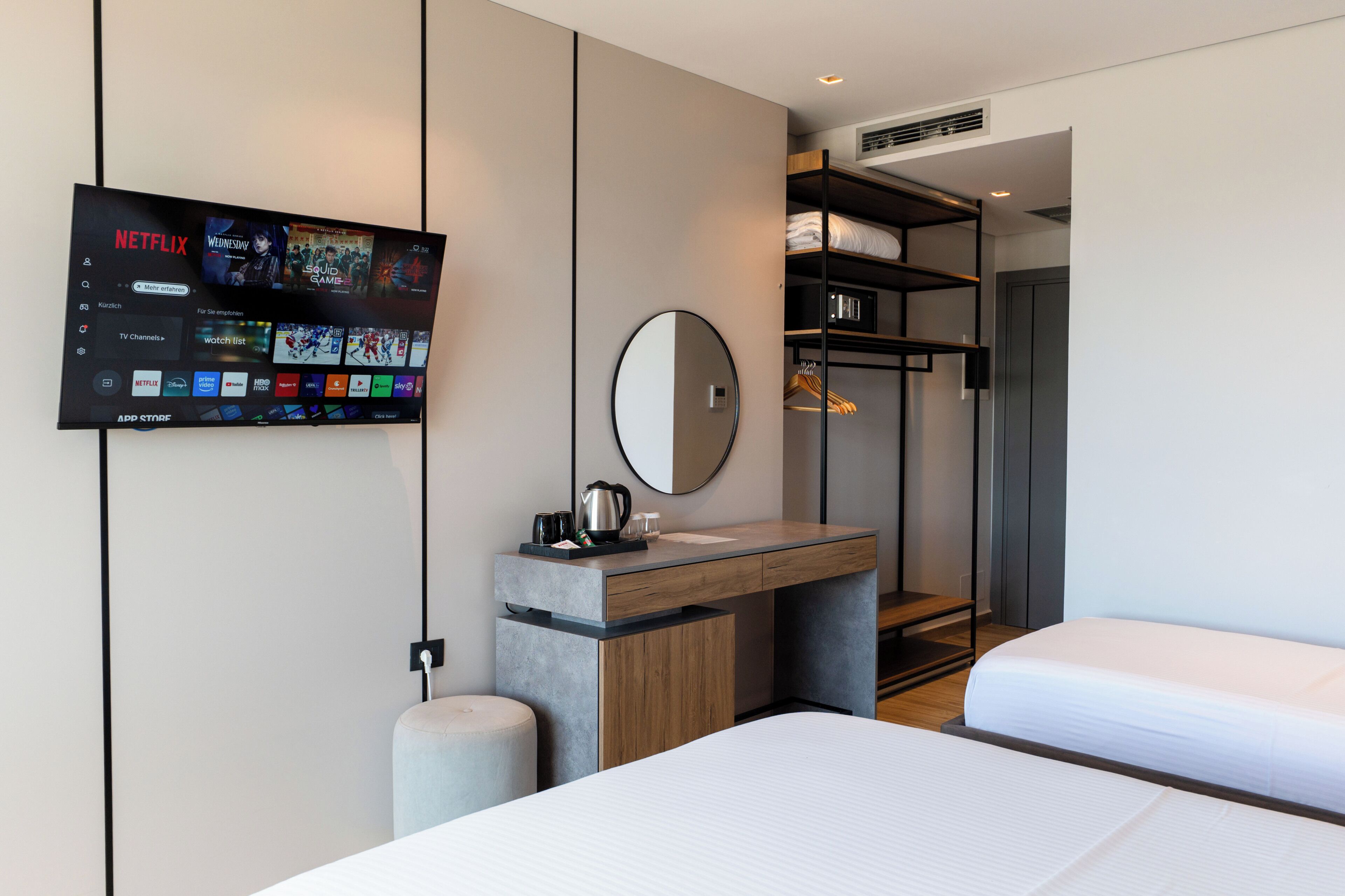 Et moderne hotelværelse med et fladskærms-tv, der viser Netflix, et træskrivebord med et spejl, en seng og en indbygget garderobe.