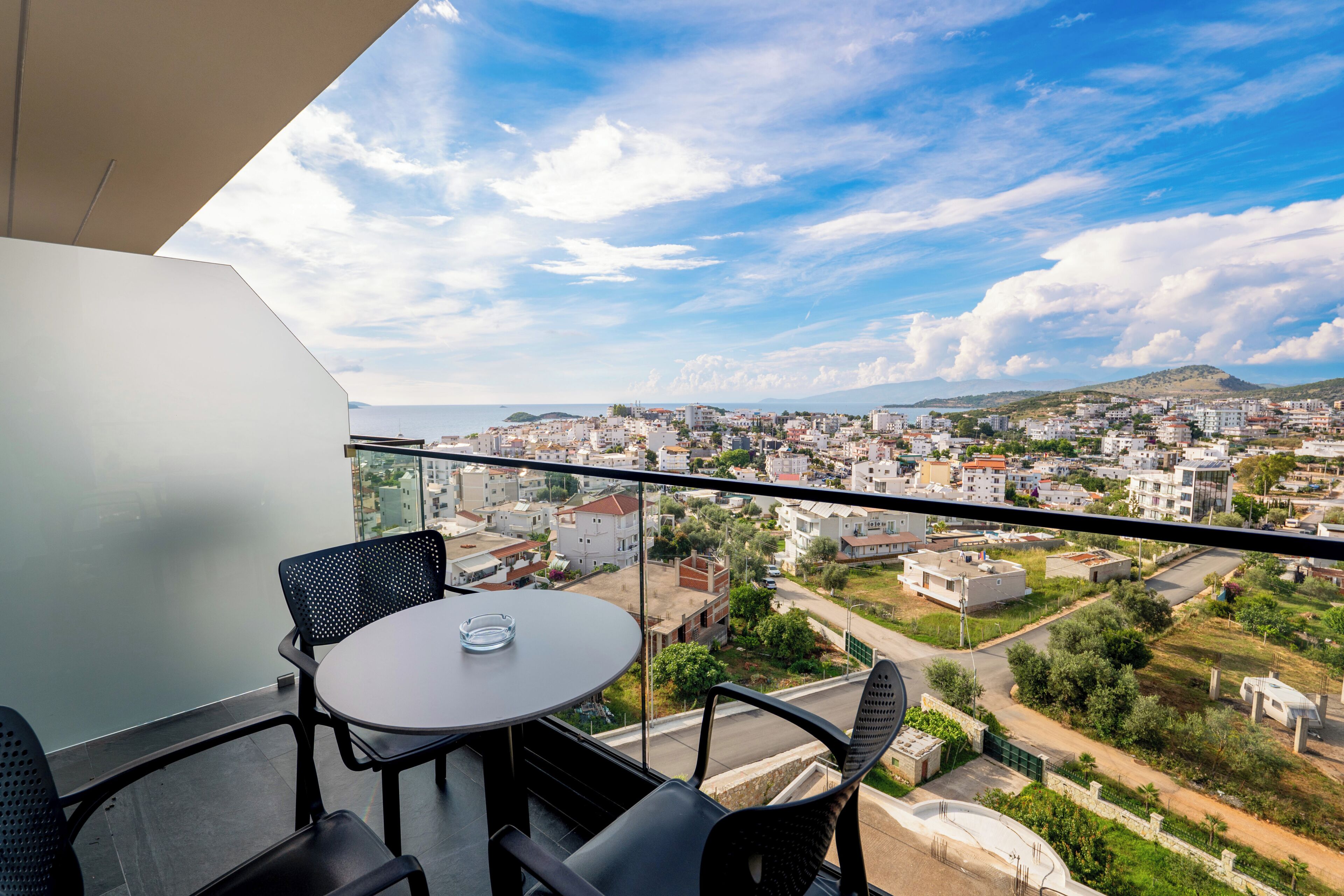 Un balcón con mesa y sillas, con vistas a un paisaje urbano con edificios y áreas verdes.