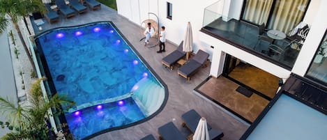 Una piscina en la azotea con sillas de descanso, un jacuzzi y barandilla de vidrio.