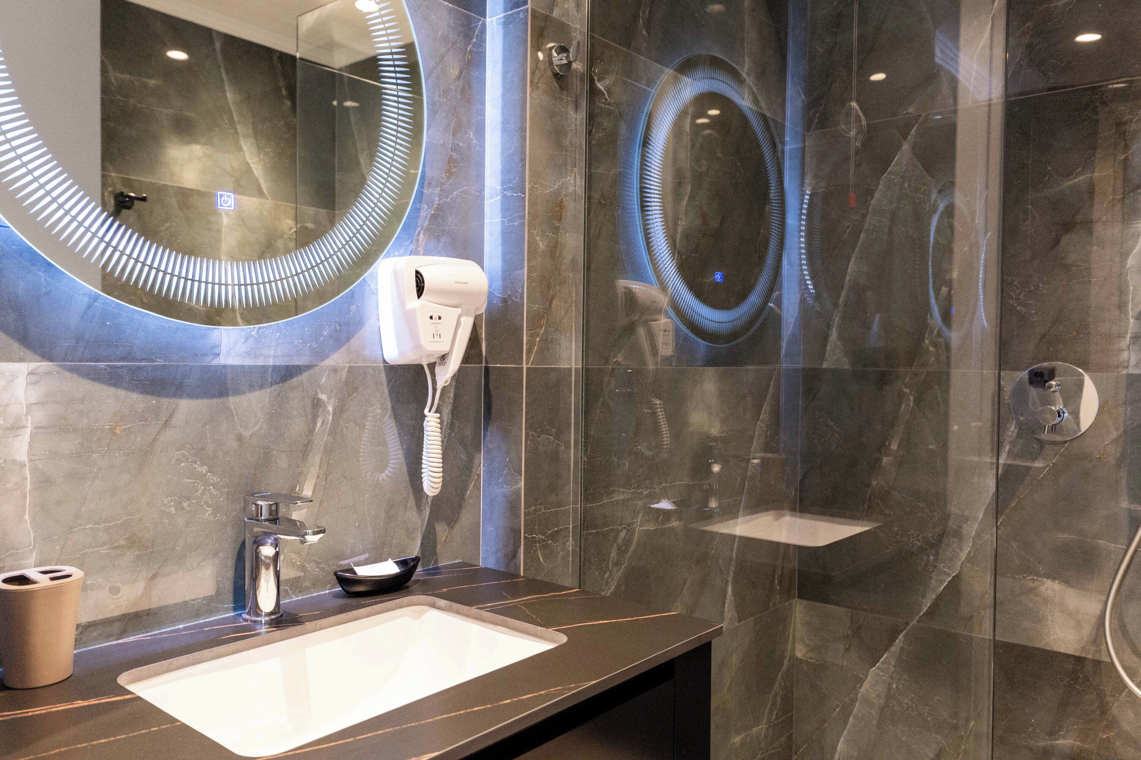 A modern bathroom with a large mirror, a hairdryer, and a sink.