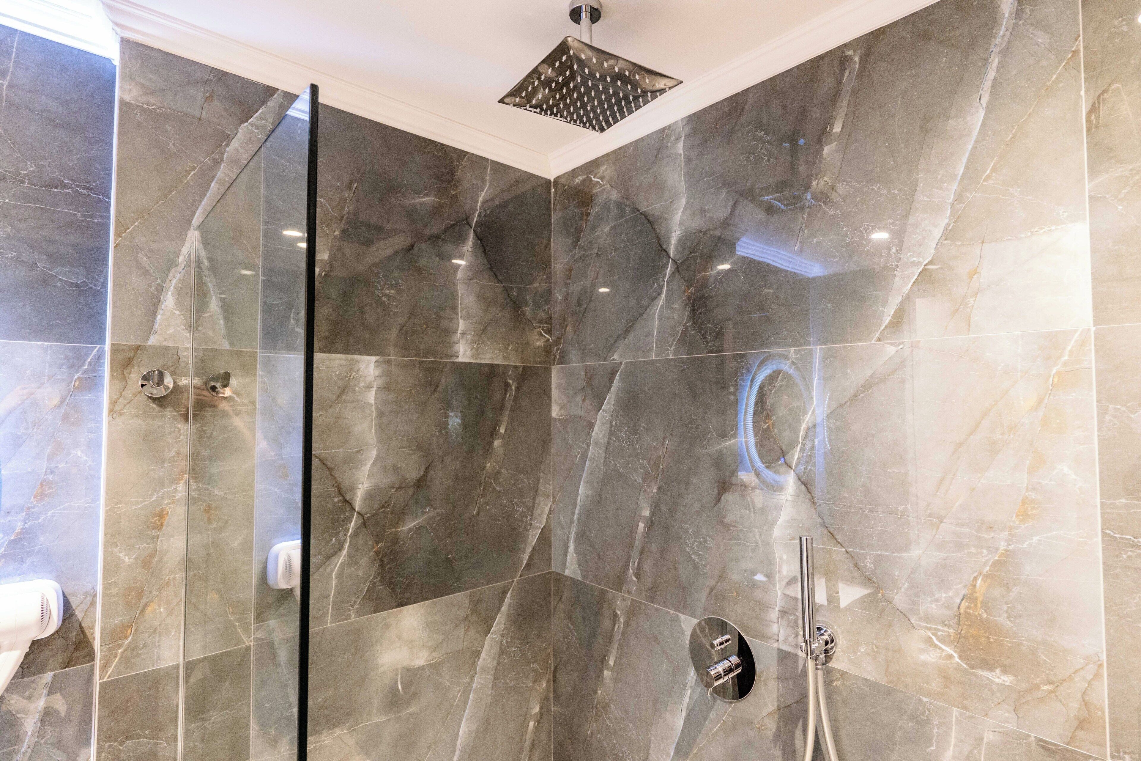 A modern bathroom with a glass shower enclosure, a handheld showerhead, and a wall-mounted faucet.