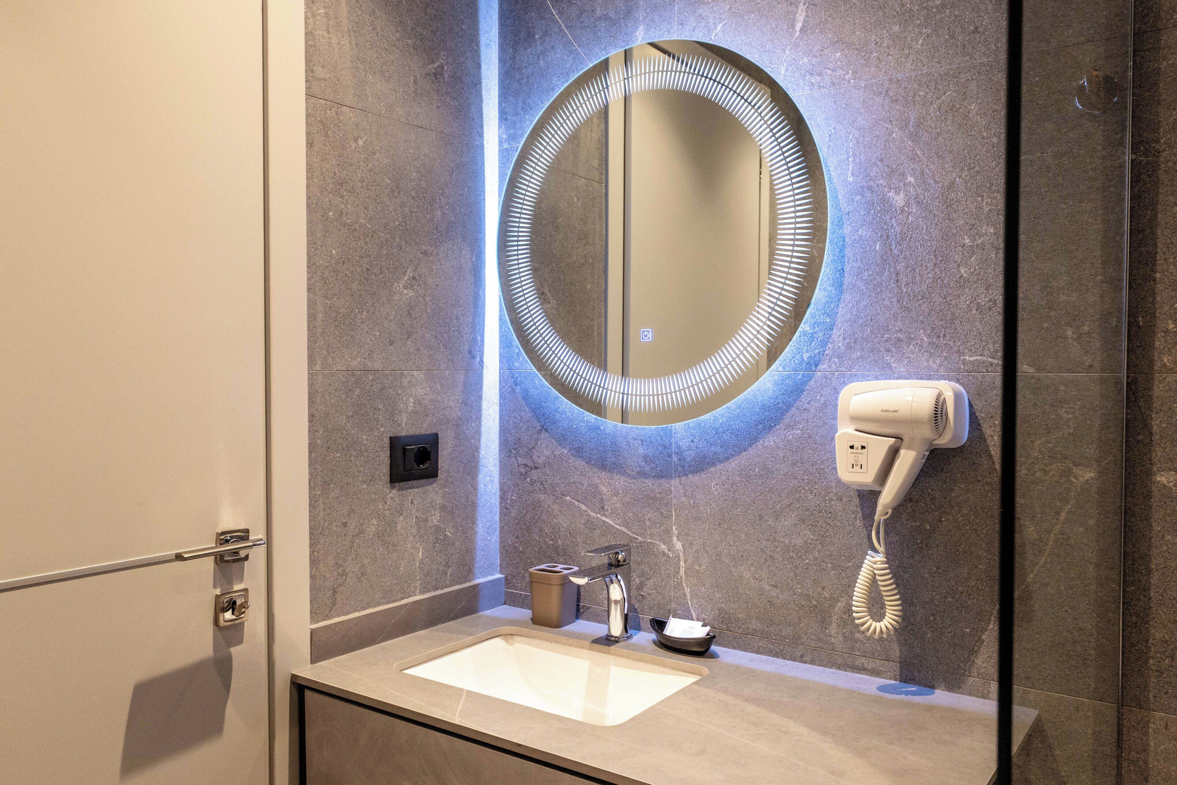 Un baño con un espejo redondo, un secador de pelo y un lavabo.