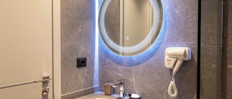 Un baño con un espejo redondo, un secador de pelo y un lavabo.
