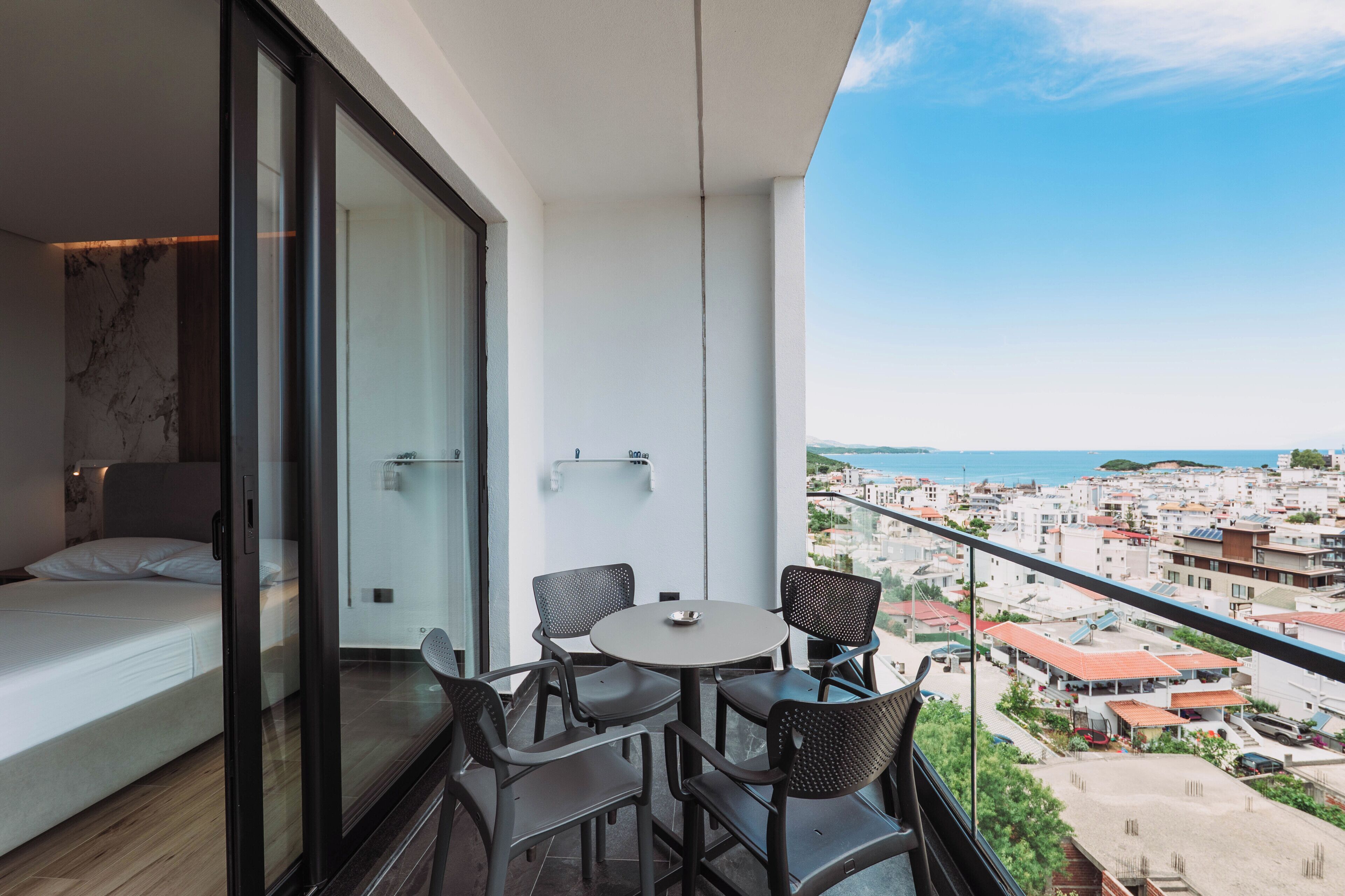 Un balcón con cama, una mesa y sillas, con vista a un pueblo costero.