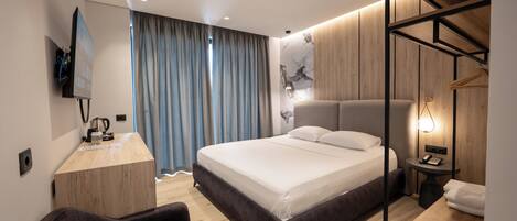 A modern hotel room with a large bed, a desk, a TV, and a wardrobe.