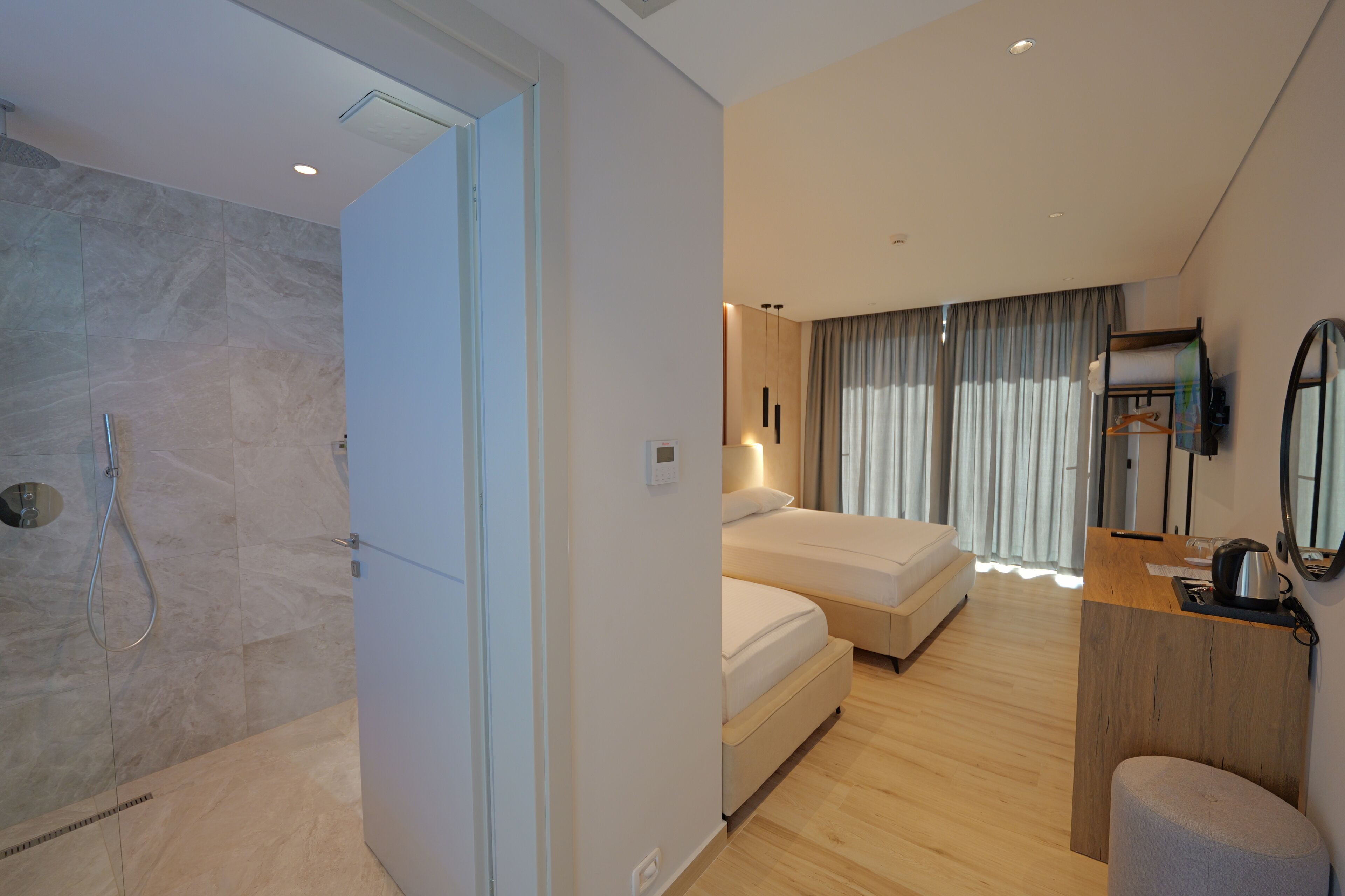 A modern hotel room with a shower, a bed, a desk, and a mirror.