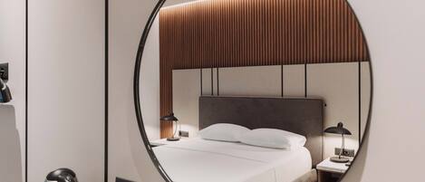 A hotel room with a bed, bedside tables, a mirror, and a kettle.
