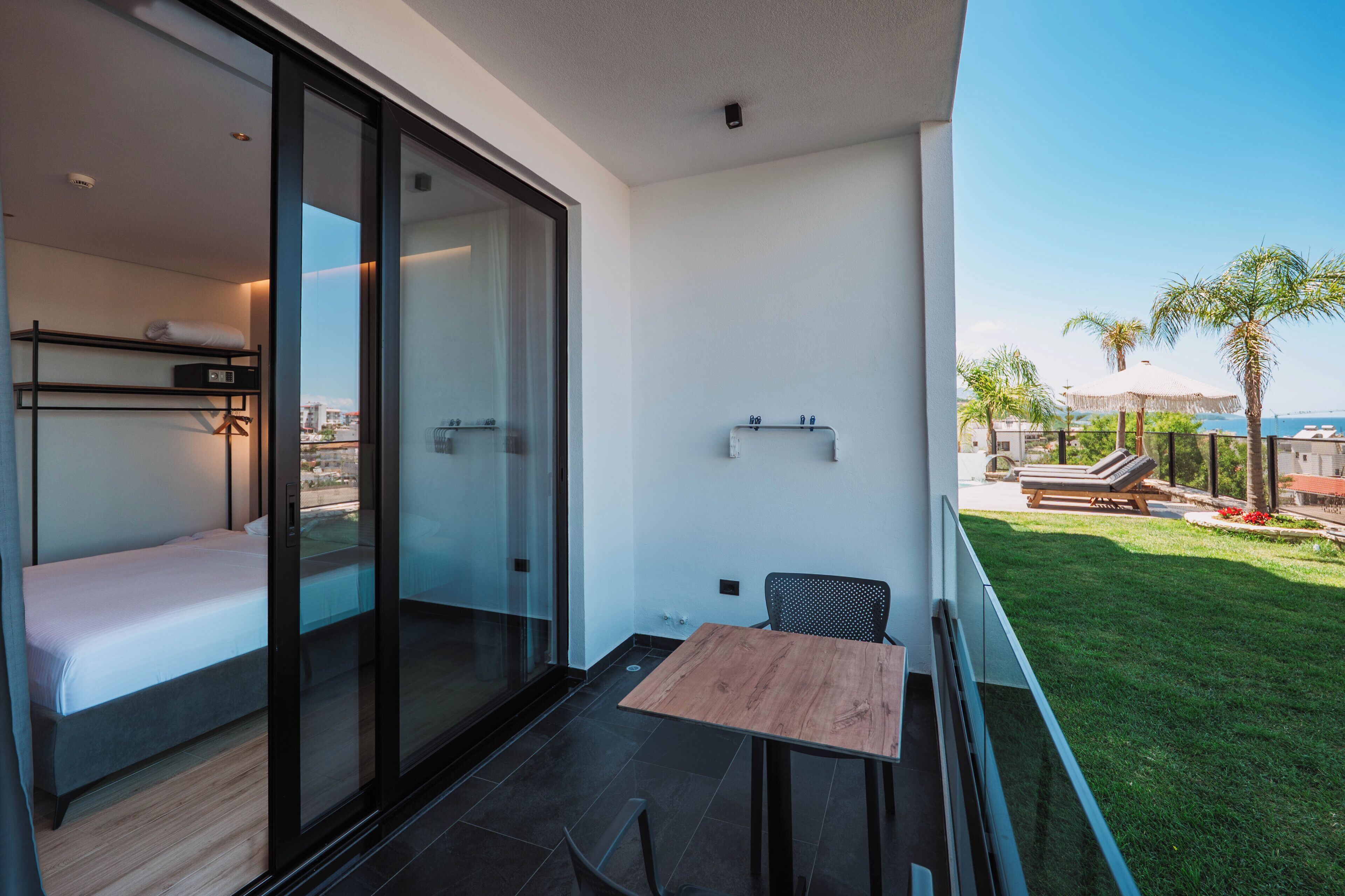 A modern room with a bed, a glass door leading to a balcony, a small table, and a chair.