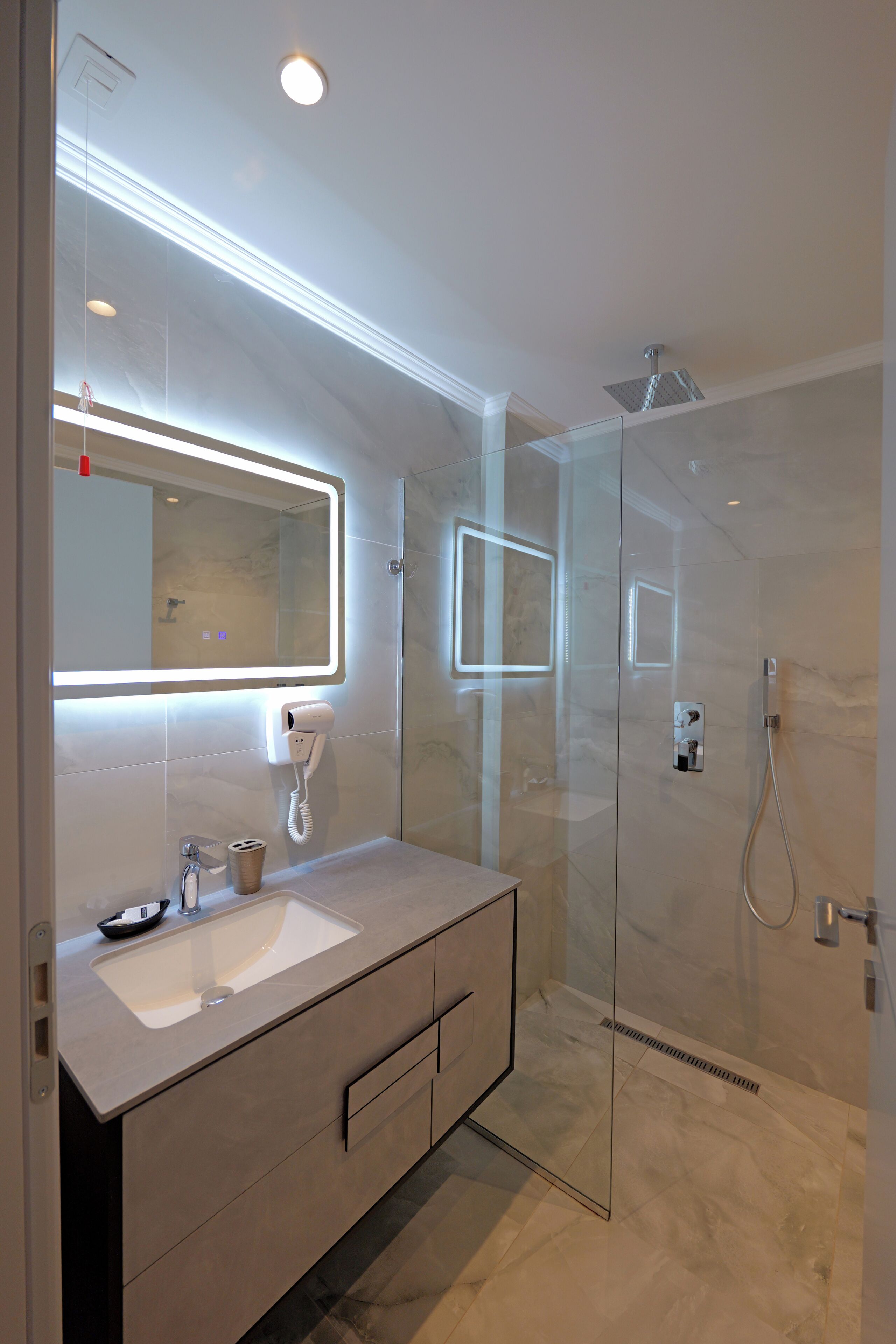 A modern bathroom with a glass shower enclosure, a built-in sink, and a mirror with integrated lighting.