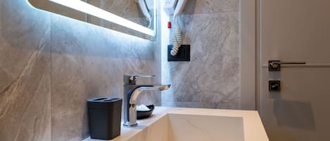 Uma casa de banho moderna com uma pia de mármore, um secador de cabelo preso à parede e um espelho com luz.