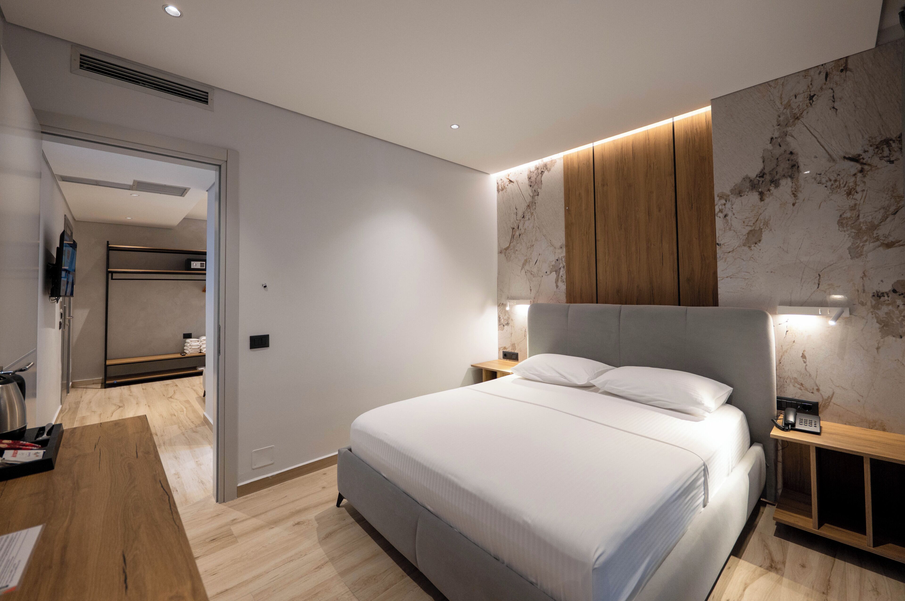 Een moderne slaapkamer met een groot bed, nachtkastjes, een houten hoofdbord en een accentmuur van marmer.